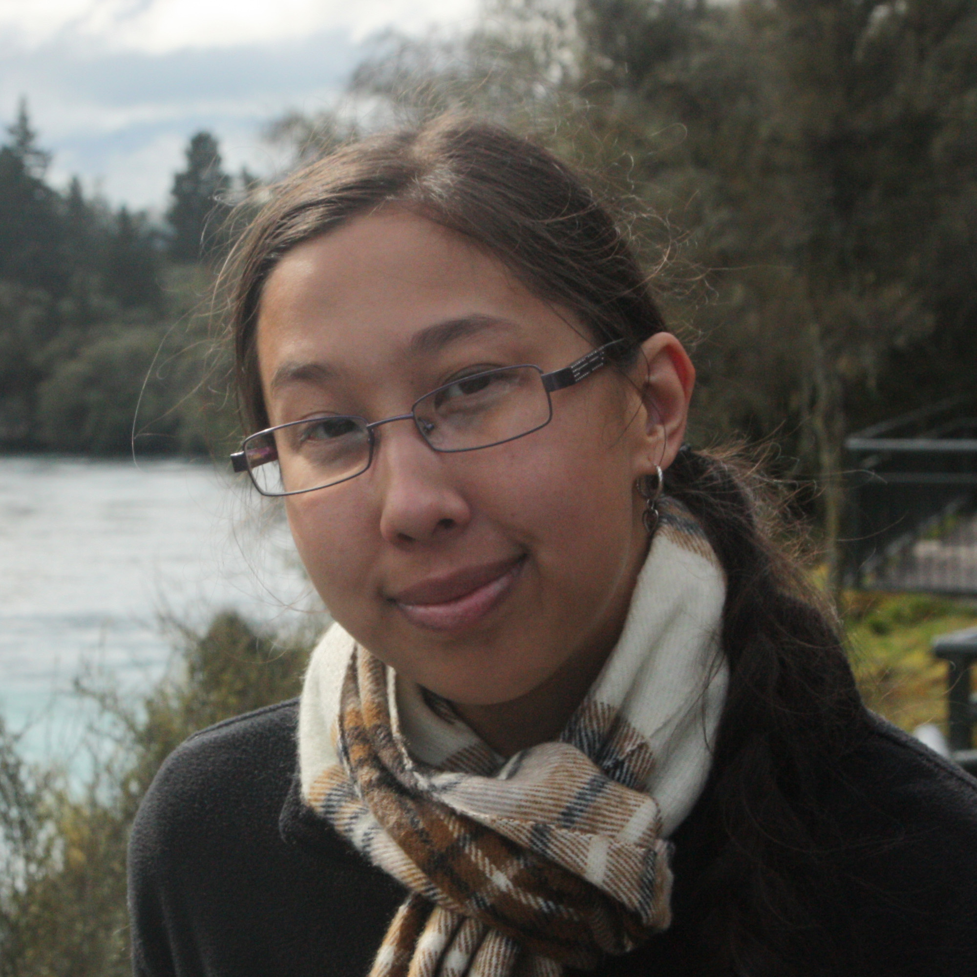 Photo of Erin, a young Asian woman with glasses, smiling by a lake 